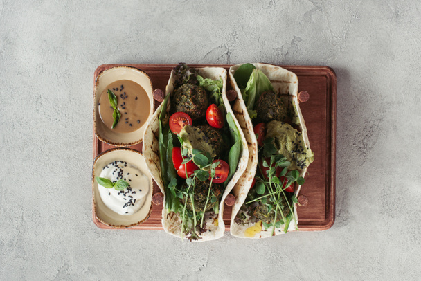 top view of falafel with tortillas, cherry tomatoes and germinated seeds of sunflower served on wooden board on grey surface - Photo, Image