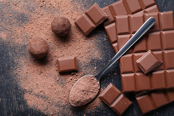 Chocoladestukjes met cacaopoeder in lepel op houten tafel - Foto, afbeelding