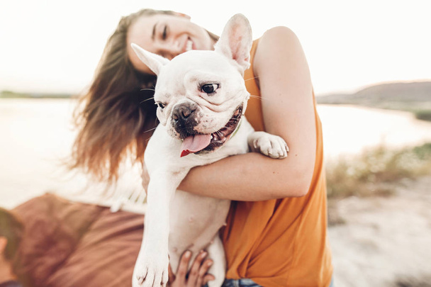 boldog csípő nő a naplemente fény, nyaralás a tengerparton bulldog játszik. Vicces kutya nyugalmi, átölelve és szórakozás a nap, stílusos lány aranyos pillanatok. hely a szöveg - Fotó, kép