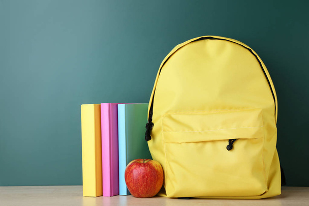 Yellow backpack with books and apple on green background - Valokuva, kuva