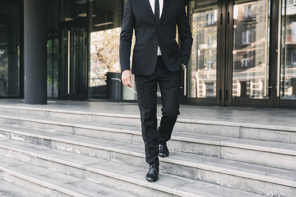 Cropped image of a businessman dressed in suit walking down the stairs outside a glass building - Фото, изображение