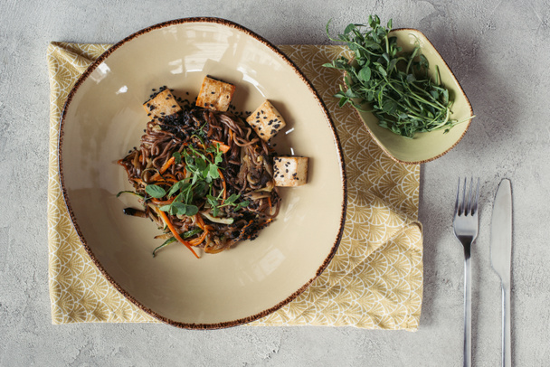 food composition with sprouts in bowl, soba with tofu and vegetables decorated with germinated seeds of sunflower on grey tabletop - Photo, Image