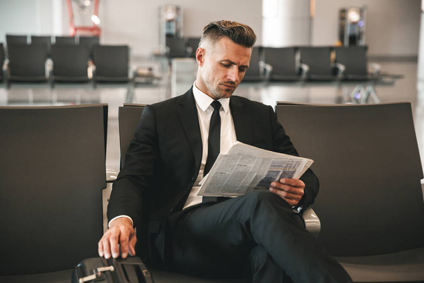 Confident businessman reading newspaper while sitting at the airport terminal lobby - Valokuva, kuva