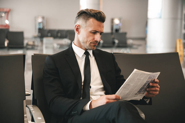Successful businessman reading newspaper while sitting at the airport terminal lobby - Фото, изображение