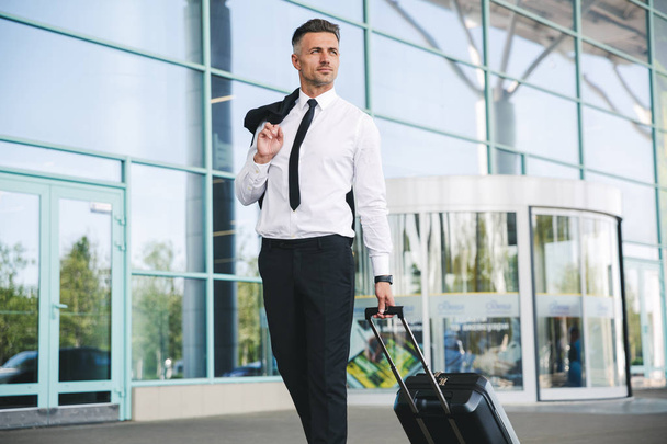 Handsome mature businessman walking outside the airport with a suitcase - Zdjęcie, obraz