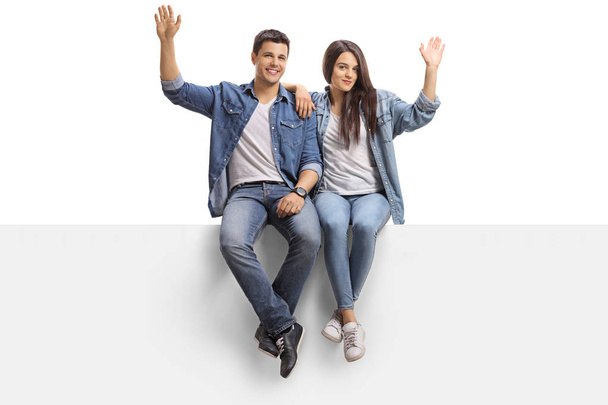 Young couple sitting on a panel and waving at the camera isolated on white background - Photo, Image
