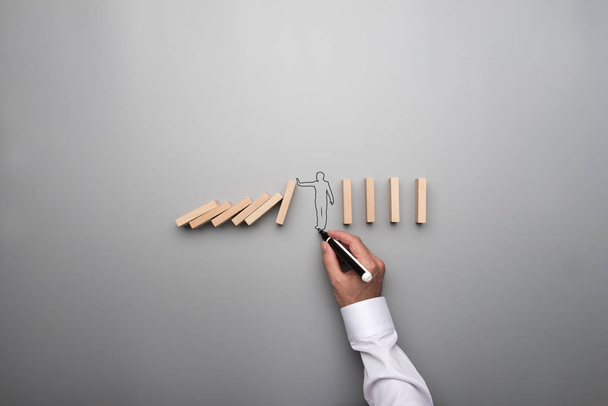 Man drawing the outline of a businessman stopping the domino effect in a conceptual image on gray background. - Photo, Image