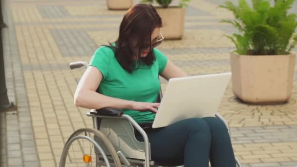 Concept of a young attractive woman business worker in a wheelchair typing on a laptop,slow mo - Кадри, відео