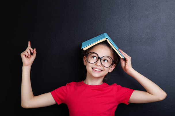 Young girl with book and glasses on blackboard background - Foto, Imagen