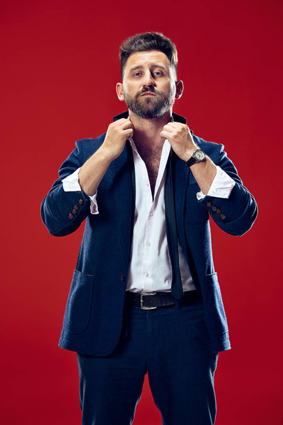 Male beauty concept. Portrait of a fashionable young man with stylish haircut wearing trendy suit posing over red background. - Foto, Bild