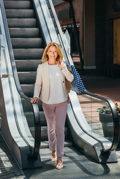 beautiful woman standing near escalator with shopping bags in mall - Φωτογραφία, εικόνα