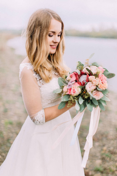 Half-length side portrait of the blonde bride holding the wed bouquet on the beach. - Fotoğraf, Görsel