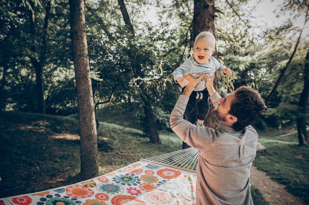 stylish dad with kid relaxing in forest and smiling, having fun. space for text. family vacation - Foto, afbeelding