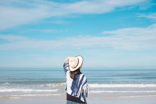 traveler young woman in casual dress with hat standing alone on beach has blue sky and sea background - Photo, Image