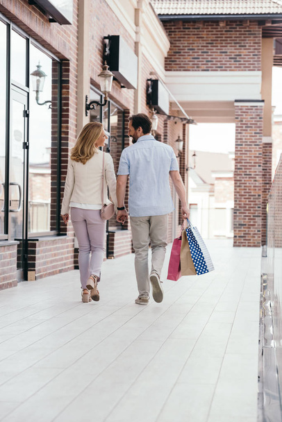 Achteraanzicht van paar, houdend handen en wandelen met shopping tassen - Foto, afbeelding
