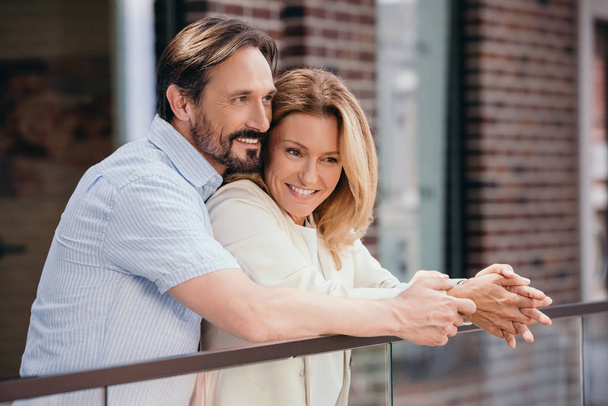 счастливая пара обнимается на балконе и смотрит в сторону
 - Фото, изображение