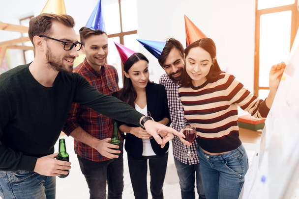 Young company workers are talking near a white board. They celebrate a corporate holiday and are dressed in holiday caps and have fun. - Foto, Imagem