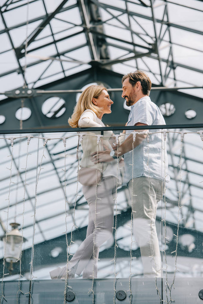 vista de ángulo bajo de la pareja de pie en el balcón del centro comercial y mirándose entre sí
 - Foto, Imagen