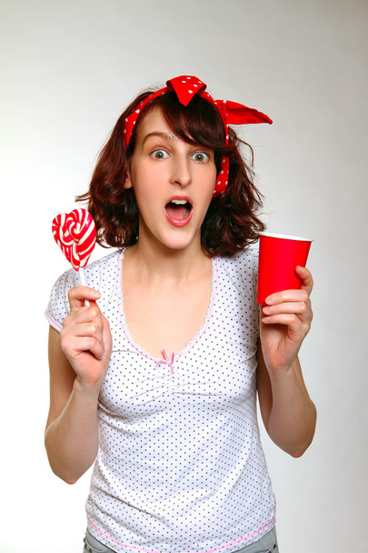Surprised girl with a lollipop and a cup isolated on a gray back - Foto, Imagen