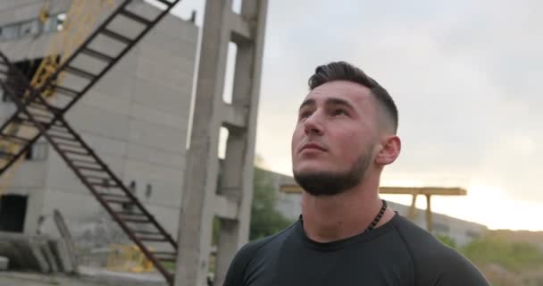 Close up portrait of healthy young sport man standing outdoors in industrial urban park and looking away. Confident young man ready of workout. - Filmagem, Vídeo