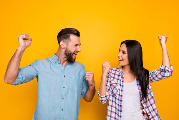 Portrait of joyful successful couple with raised arms looking at each other yelling celebrating achievement isolated on bright yellow background - Photo, image