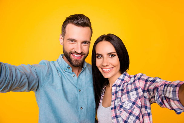 Self portrait of lovely attractive couple hugging shooting selfie on front camera having beaming smiles wearing casual shirts isolated on vivid yellow background - Valokuva, kuva