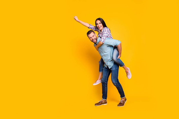 Full size portrait of playful carefree couple in piggy back style making super man sign with raised fist isolated on bright yellow background - Foto, immagini