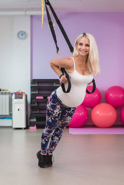 junge schwangere attraktive Frau trainiert mit Trageschlaufen im Fitnessstudio - Foto, Bild