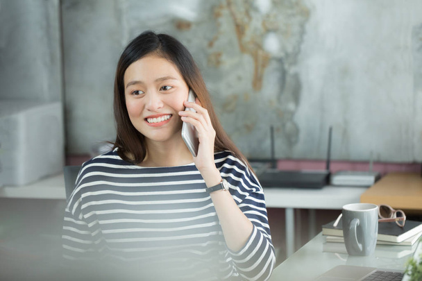 Young Asian business woman using smartphone to interact with customers in office. - Photo, Image
