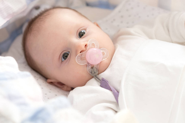 Portrait of cute baby girl with pacifier lying in her crib - Foto, imagen