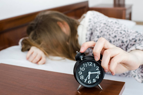 Young woman girl turns off alarm clock waking up in the morning from a call. Unrecognizable student do not want to wake up early for school or univercity. Oversleep, not getting enough sleep concept. - Foto, Bild