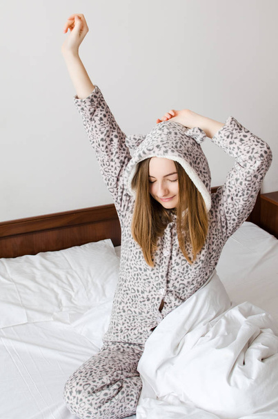 Gelukkig jonge vrouw genieten van zonnige ochtend. Kaukasische meisje in leuke warme pyjama die zich uitstrekt in het bed en lachend na het wakker worden. Goede start van de dag-concept. - Foto, afbeelding