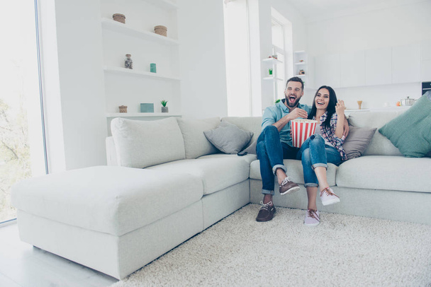 Ha-ha! Happiness joy pleasure enjoyment cinema concept. Full size portrait of positive laughters watching funny comedy eating snack sitting on sofa in modern white living room - Фото, изображение
