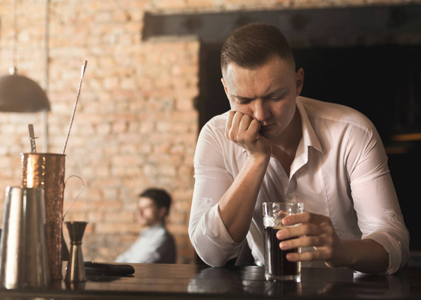 Sad young man looking at glass of beer at bar - Zdjęcie, obraz
