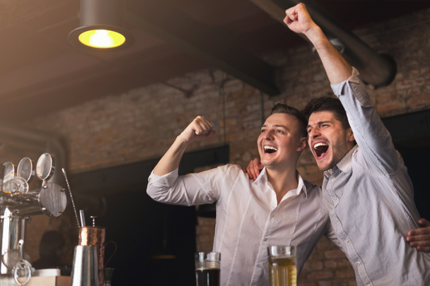 Happy friends cheering for favorite team in pub - Photo, image