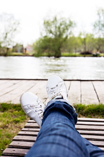 female legs in a sneaker on a lounger against the background of the river and forest - Photo, Image