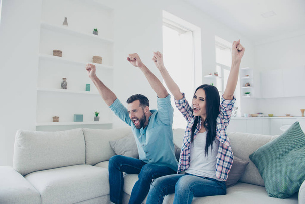 Inspiration motivation concept. Portrait of excited active couple holding raised hands yelling celebrating victory of favorite football team enjoying leisure together sitting on sofa indoor - Photo, Image