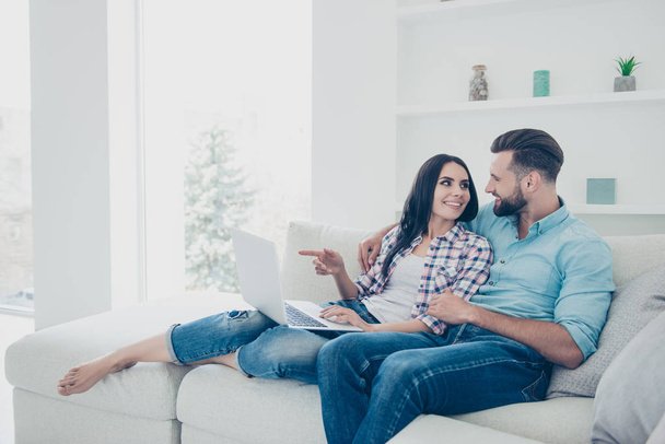Portrait of stylish modern couple choosing goods in internet shop gesturing with forefinger enjoying online shopping sitting on sofa in living room - Photo, image