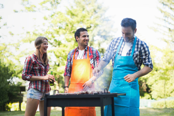 Young happy people enjoying barbecuing in forest - Foto, Imagen
