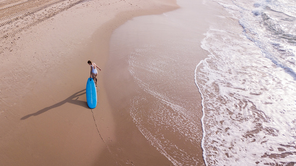 aerial view of woman in white swimsuit pulling surfboard on sandy beach, Ashdod, Israel - Photo, Image