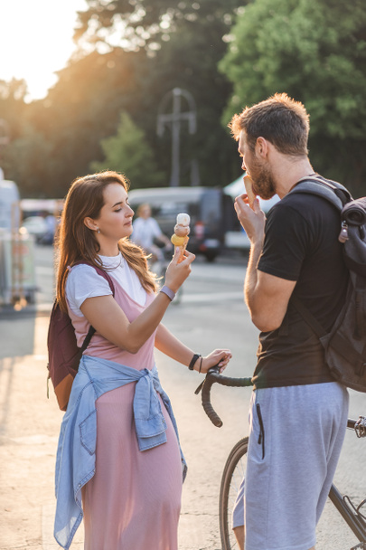 young man with bicycle eating ice cream while his girlfriend standing near at street - Foto, imagen