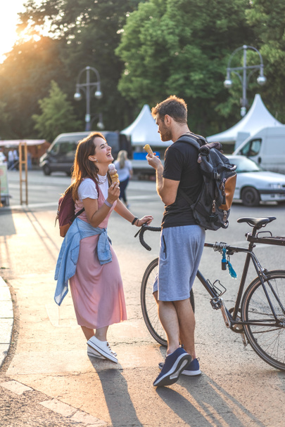 sorrindo casal com bicicleta comendo sorvete e conversando uns com os outros na rua urbana
 - Foto, Imagem
