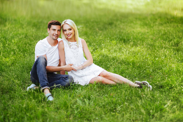 The lovely beautiful couple in love sitting on green grass. Romantic love story in the park. Young girl and boy in love. - Photo, Image