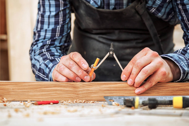 Un primer plano de un carpintero masculino marcas de una brújula de metal y un lápiz en una barra de madera para hacer muebles
. - Foto, Imagen