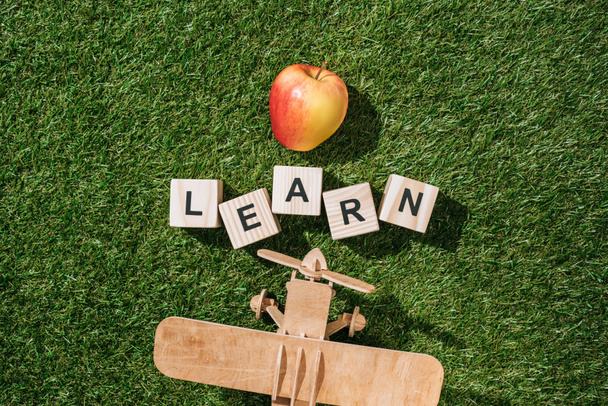 vista superior de avión de juguete de madera, manzana fresca y aprender inscripción hecha de bloques en hierba verde
 - Foto, Imagen