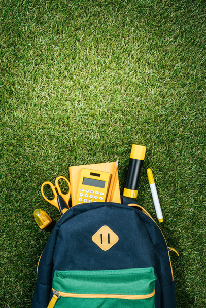 flache Liege mit geordnetem Rucksack und Schreibwaren auf grünem Gras - Foto, Bild