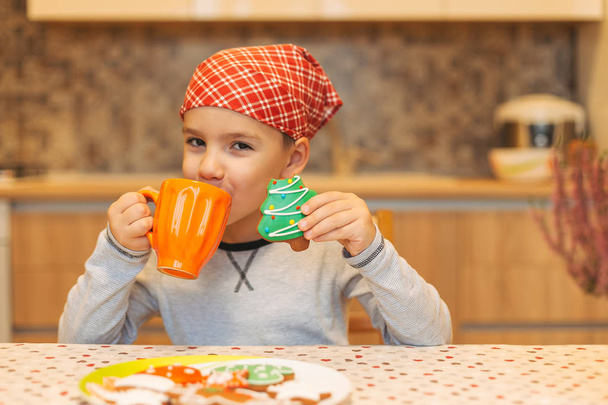 Χαριτωμένο ευτυχισμένο αγόρι, πίνοντας τσάι και τρώγοντας τα cookies - Φωτογραφία, εικόνα