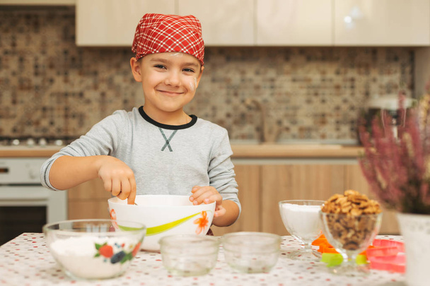 Симпатичный мальчик готовит на кухне дома, глядя в камеру
 - Фото, изображение