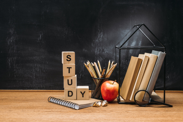 close up view of study inscription made of wooden blocks, notebook, fresh apple and books on surface with empty blackboard behind - Fotografie, Obrázek