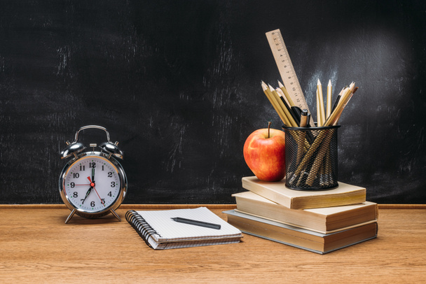 vista da vicino di mela fresca, orologio, quaderno, matite e libri su tavolo in legno con lavagna vuota dietro
 - Foto, immagini